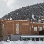 Photo of the Park City Library building from the North. A three story historic brick building with a newer first level that has a patio. Snow covers the Library Field that is located North of the building.
